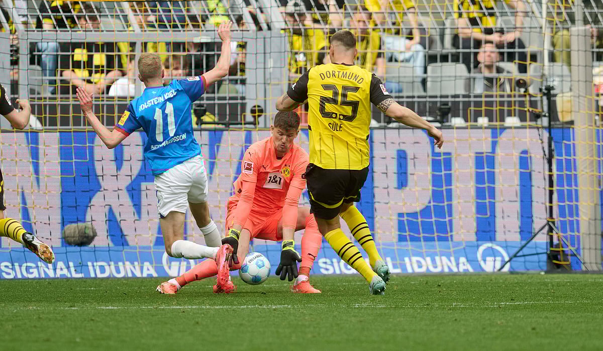 Bernd Thissen/dpa via AP : Dortmund goalkeeper Gregor Kobel, center, and Niklas Suele in action against Kiel's Alexander Bernhardsson during the German Bundesliga soccer match between Borussia Dortmund and Holstein Kiel at Signal Iduna Park in Dortmund, Germany.
