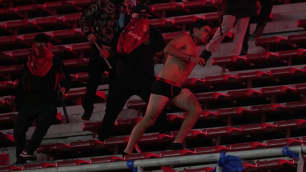 | Photo: AP/Gustavo Garello : Fans of Argentina’s Independiente attack a Universidad de Chile fan, right, after they stripped him of his clothing during a Copa Sudamericana round of sixteen second leg soccer match at the Libertadores de America stadium in Avellaneda, Argentina, Wednesday, Aug. 20, 2025.