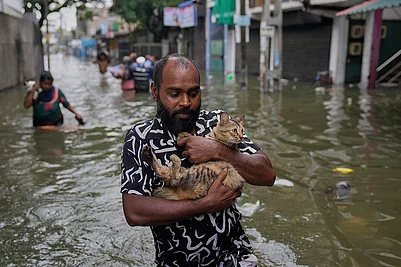 | Photo: AP/Eranga Jayawardena : A man wades through a flooded road carrying a cat in Colombo, Sri Lanka.