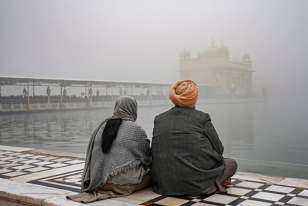| Photo: PTI/Shiva Sharma : Devotees sit near the Amrit Sarovar at Golden Temple amid dense fog, in Amritsar.