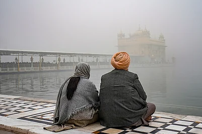 | Photo: PTI/Shiva Sharma : Devotees sit near the Amrit Sarovar at Golden Temple amid dense fog, in Amritsar.