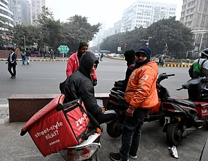 Source: IMAGO / Hindustan Times : Gig workers rest during a nationwide strike at Connaught Place on December 31, 2025 in New Delhi, India. Gig workers are striking on New Years Eve, demanding better pay, social security, and an end to 10-minute delivery mandates due to safety concerns and stress. While the strike aimed to disrupt high-demand New Years Eve services, the overall impact was mitigated by aggressive counter-measures from delivery platforms.