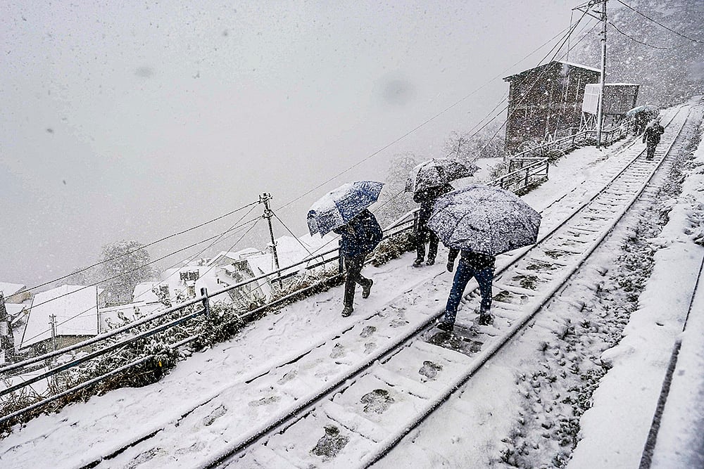 | Photo: PTI : People traverse a snow-covered rail track amid ongoing snowfall, in Shimla. The precipitation aligns with forecasts predicting up to 28 cm of snow on January 23, ending the regions dry spell under active western disturbances.
