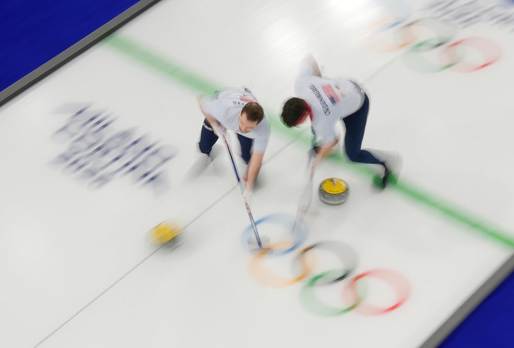 | Photo: AP/David J. Phillip : United States Aidan Oldenburg and Luc Violette sweep ahead of a stone during a mens curling round robin match against Canada at the 2026 Winter Olympics, in Cortina dAmpezzo, Italy, Friday, Feb. 13, 2026. 