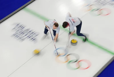 | Photo: AP/David J. Phillip : United States Aidan Oldenburg and Luc Violette sweep ahead of a stone during a mens curling round robin match against Canada at the 2026 Winter Olympics, in Cortina dAmpezzo, Italy, Friday, Feb. 13, 2026.