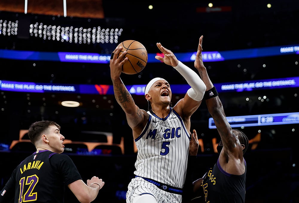 | Photo: AP/Caroline Brehman : Orlando Magic forward Paolo Banchero (5) drives to the basket with the ball while being guarded by Los Angeles Lakers forward Jake LaRavia (12) and Los Angeles Lakers center Deandre Ayton (5) during the first half of an NBA basketball game in Los Angeles. 