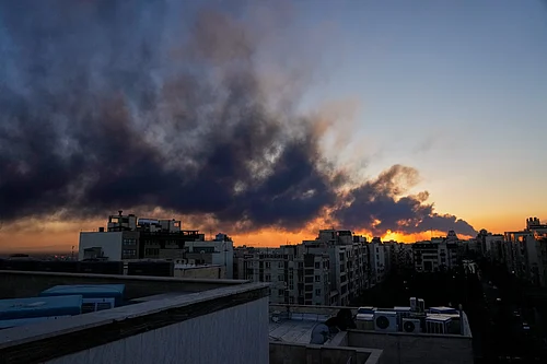 AP News : The sun sets behind a plume of smoke rising after a U.S.–Israeli military strike in Tehran, Iran, Tuesday, March 3, 2026.