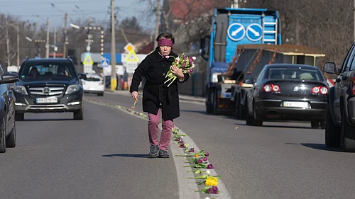 Credit: AP Photo/Efrem Lukatsky : A villager lays flowers on a road in the village of Novi Petrivtsi close to capital Kyiv, Ukraine, Thursday, March 12, 2026, ahead of a funeral procession for a Ukrainian army soldier who was killed in a battle with Russian troops.