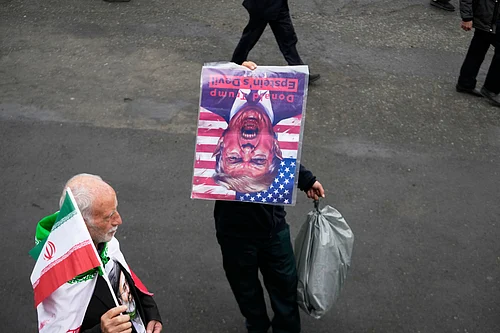 AP Photo/Vahid Salemi : A man holds a picture of U.S. President Donald Trump upside down after Friday prayers at the Imam Khomeini Grand Mosque in Tehran, Iran, Friday, March 20, 2026