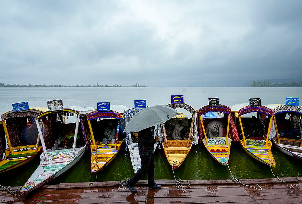 | Photo: PTI/S Irfan : A man walks past shikaras holding an umbrella during rainfall at Dal Lake, in Srinagar.