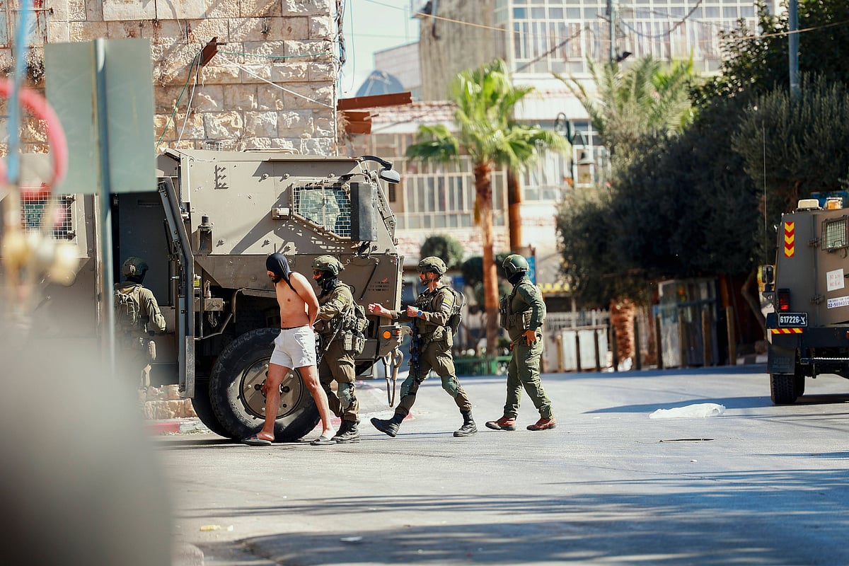 Credit: IMAGO / Middle East Images : Israeli Raid In Al Birah West Bank Israeli soldiers escort a detained man near a military vehicle in Al Birah, West Bank on October 7, 2025
