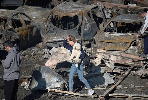 | Photo: AP/Emilio Morenatti : A woman holds her dog as she walks past burned cars a day after an Israeli airstrike in Beirut, Lebanon, Thursday, April 9, 2026.