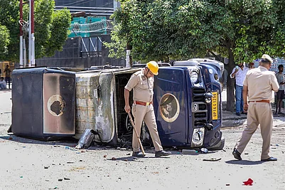 | Photo: PTI : Police personnel inspect the wreckage of a vehicle during a protest by factory workers demanding a hike in wages, in Noida, Gautam Buddh Nagar district, Uttar Pradesh. The protest carried incidents of arson, vandalism and stone-pelting reported from Phase-2 and Sector 60 areas, police said.