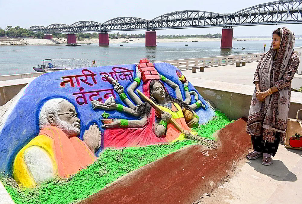 | Photo: PTI : A woman looks at a sand art carved by Sand artist Rupesh Singh dedicated on Nari Shakti Vandan Adhiniyam, commonly known as Womens Reservation Act, at Namo Ghat, in Varanasi, Uttar Pradesh.