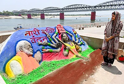 | Photo: PTI : A woman looks at a sand art carved by Sand artist Rupesh Singh dedicated on Nari Shakti Vandan Adhiniyam, commonly known as Womens Reservation Act, at Namo Ghat, in Varanasi, Uttar Pradesh.