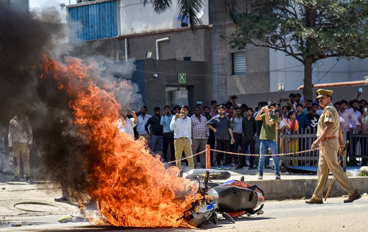 Source:  PTI : Flames billow as a police bike is set ablaze by factory workers during a protest demanding a hike in wages, in Noida, Gautam Buddh Nagar district, Uttar Pradesh, Monday, April 13, 2026. The protest carried incidents of arson, vandalism and stone-pelting reported from Phase-2 and Sector 60 areas, police said.