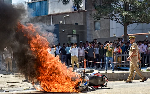 Source: PTI : Flames billow as a police bike is set ablaze by factory workers during a protest demanding a hike in wages, in Noida, Gautam Buddh Nagar district, Uttar Pradesh, Monday, April 13, 2026. The protest carried incidents of arson, vandalism and stone-pelting reported from Phase-2 and Sector 60 areas, police said.