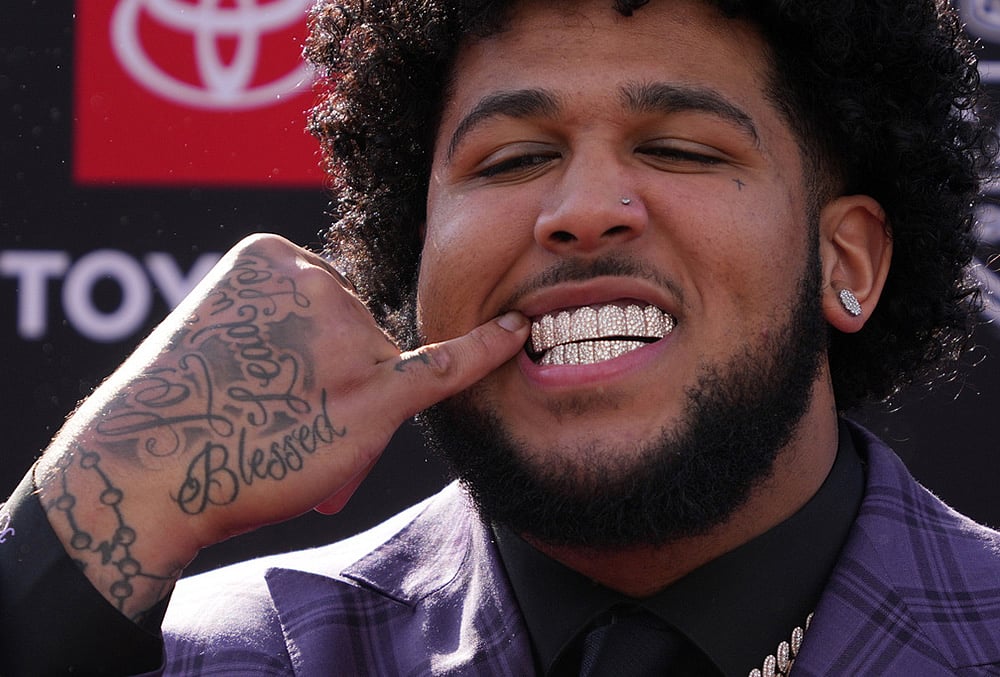 | Photo: AP/Gene J. Puskar : Alabama offensive lineman Kadyn Proctor shows off his dental jewelry while posing on the red carpet before the first round of the NFL football draft in Pittsburgh