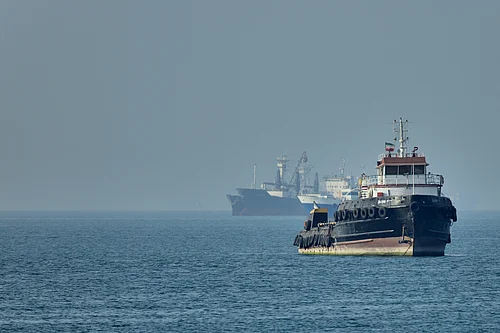 PTI : An Iranian tugboat floats in the foreground as cargo ships sit at anchor in the Strait of Hormuz off Bandar Abbas, Iran.
